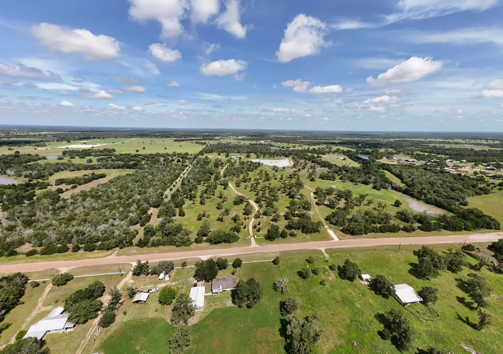 Wide aerial view of open land, trees and a road