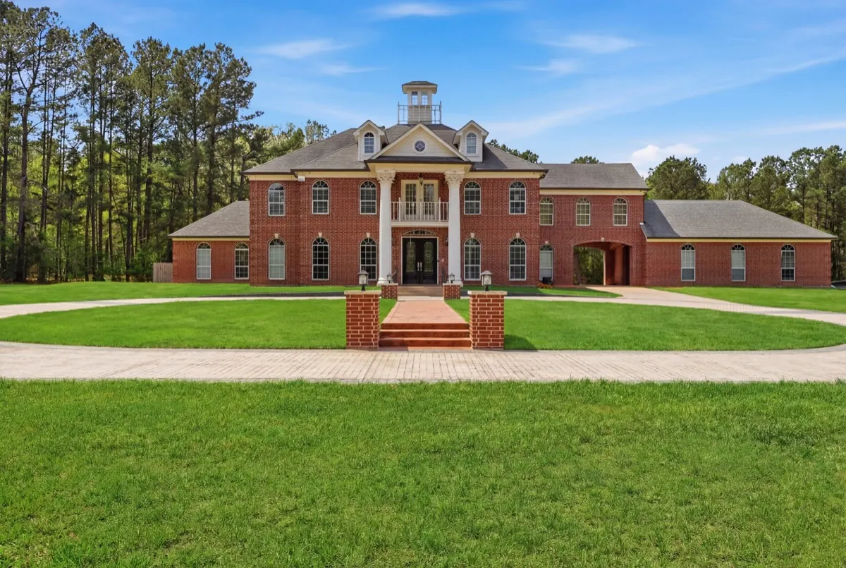 Red-brick home with a columned entrance, green lawn and surrounding trees