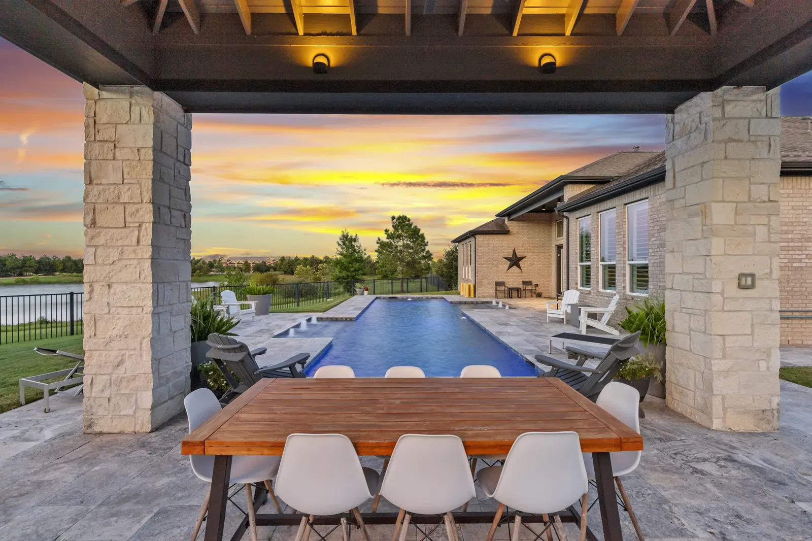 Covered outdoor dining area overlooking an illuminated pool beneath a sunset sky
