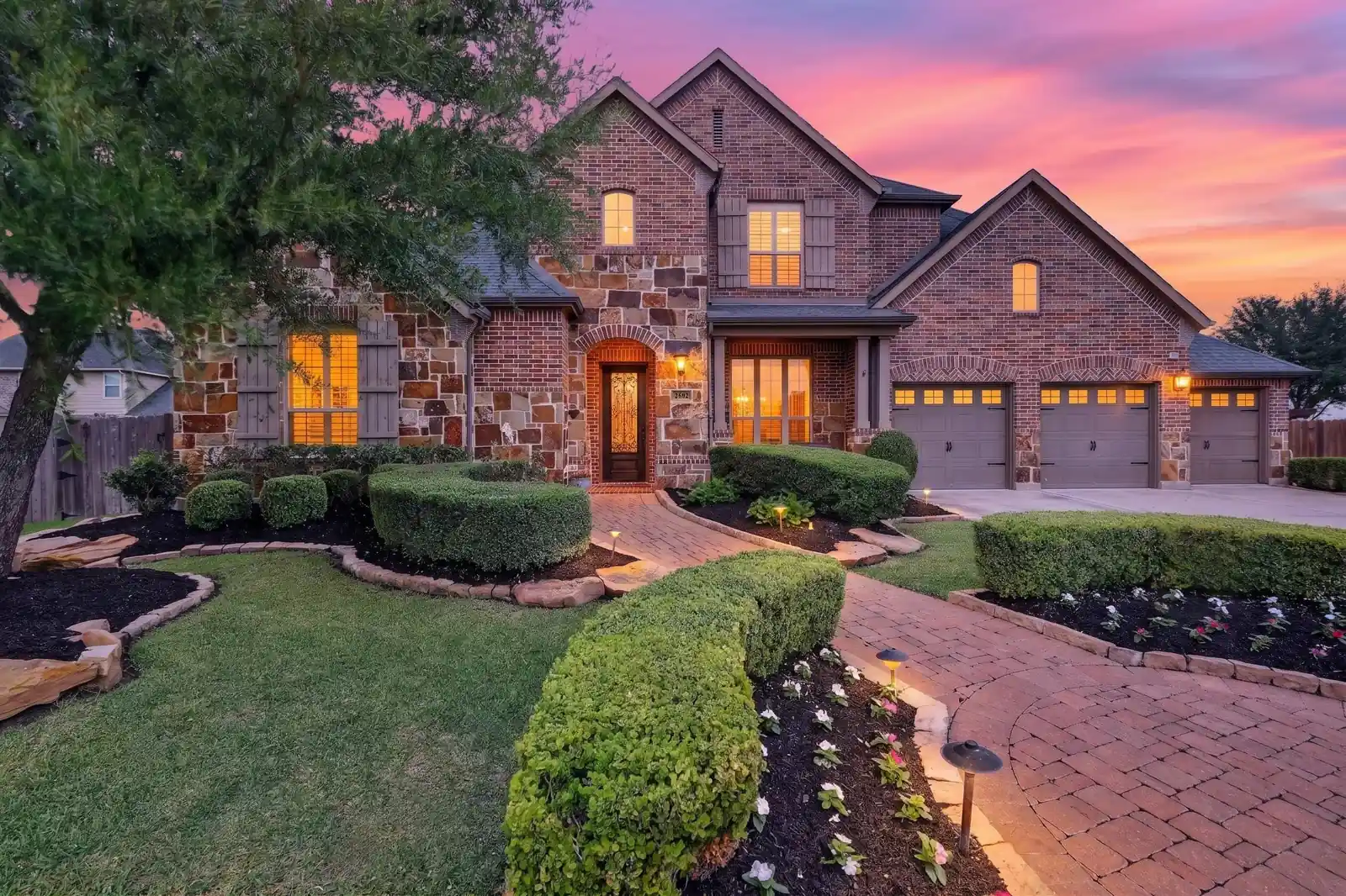 Brick home with illuminated windows beneath a colourful evening sky