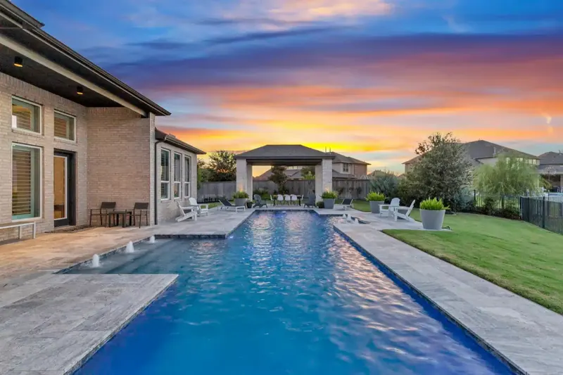 Backyard swimming pool and covered patio beneath a colorful twilight sky